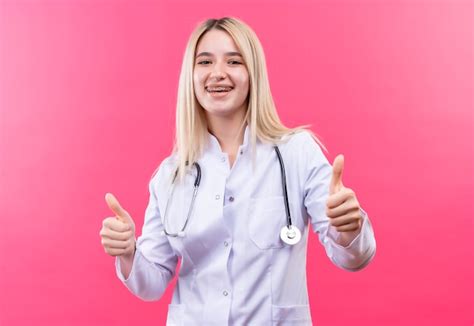 Sourire médecin jeune fille blonde portant un stéthoscope en robe médicale et appareil dentaire