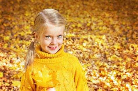 Niña feliz en el parque de otoño con hojas de arce amarillas en sus