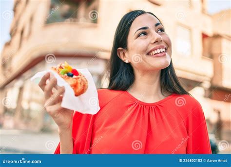 Jovencita Latina Sonriendo Feliz Comiendo Dulce Caminando Por La Ciudad Imagen De Archivo