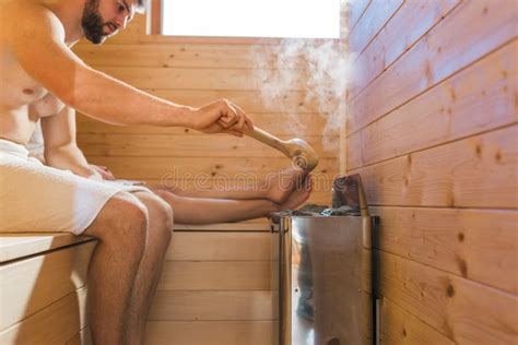 Man Pouring Water With A Wooden Ladle Spoon On Hot Rocks While Relaxing In A Sauna Stock Image