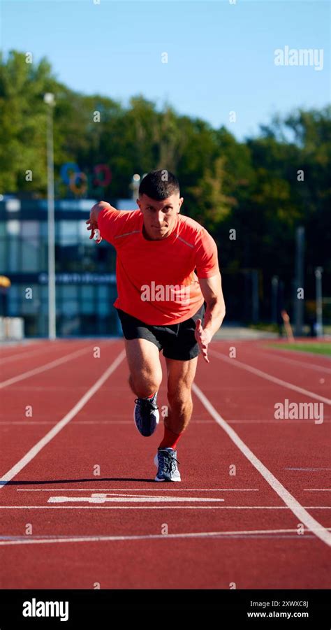 Sprinter in red shirt launches forward on track, eyes locked ahead ...