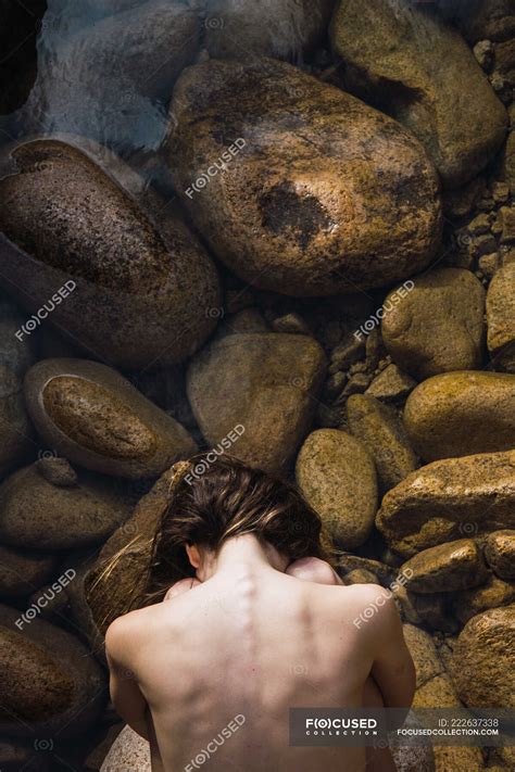 From Above Naked Woman Sitting With Hands Behind Back On Stones Posing Bare Stock Photo