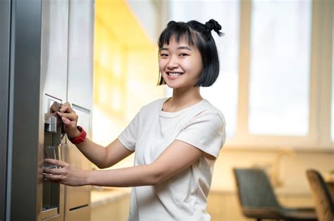 Mujer Alegre Llenando Un Vaso Con Agua De La Nevera Foto Premium