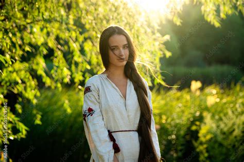 Beautiful Brunette Braided Girl In Rural Long Ukrainian Dress Posing Near River With Buckets Of