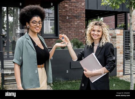 Blonde Real Estate Agent Giving Key From New House To Pleased African American Buyer Stock Photo