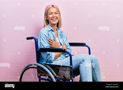 Belle femme blonde assise sur un fauteuil roulant souriant et riant fort à haute voix parce que