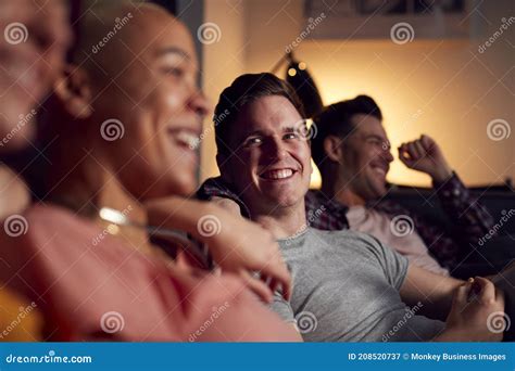 Group Of Gay Friends Sitting On Sofa At Home Watching Evening Tv And Relaxing Together Stock