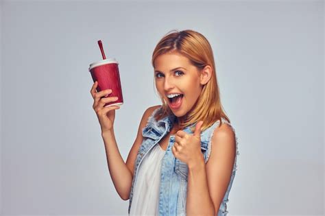 Positif et la femme blonde souriante tient une tasse de papier rouge avec du jus isolé sur fond