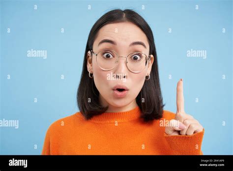 Portrait Of Smiling Brunette Asian Woman In Glasses Raises One Finger Eureka Sign Pitching An