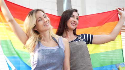 Happy Caucasian LGBT Couple Lesbian Holding And Waving Rainbow LGBT Pride Flag Together In The