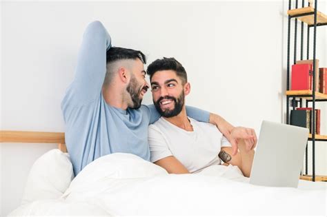 Heureux Beau Couple Gay Assis Sur Le Lit Avec Un Ordinateur Portable Photo Gratuite