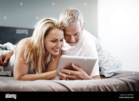 Lets Start Planning Our Weekend A Mature Couple Using A Digital Tablet While Lying In Bed Stock