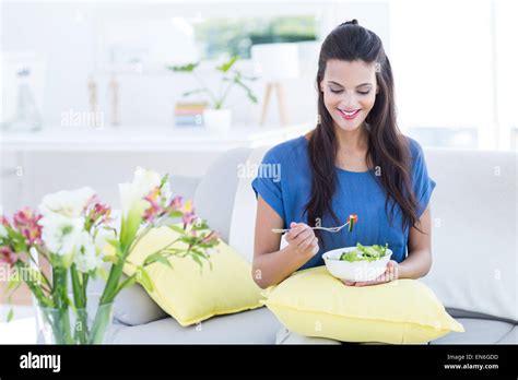 Smiling Beautiful Brunette Sitting On The Couch And Eating Salad Stock Photo Alamy