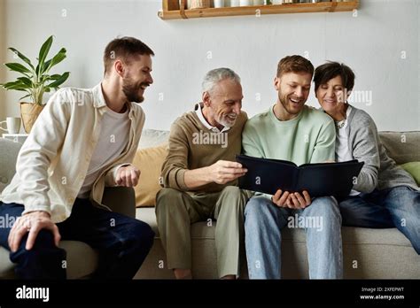 A Gay Couple Laughs With Parents While Looking At An Old Photo Album Together On The Couch Stock