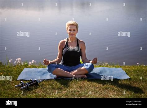 Peaceful Mature Woman Practices Yoga Outdoors Female Athlete Sitting In Lotus Position Against