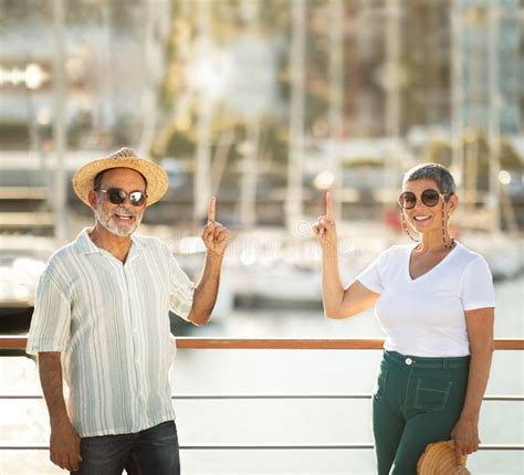 Mature Couple Pointing Fingers Up Near Yachts At Marina Outside Stock