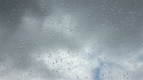 Time lapse rain drops in front of dark clouds on a glass window