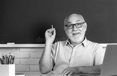 Portrait Of Mature Teacher Or Tutor Professor Working At Table In College Or School Stock Photo