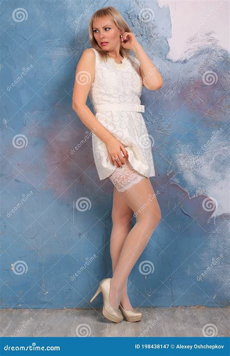 Blonde Long Legged Model In White Minidress And White Stockings Posing In Studio Stock Image