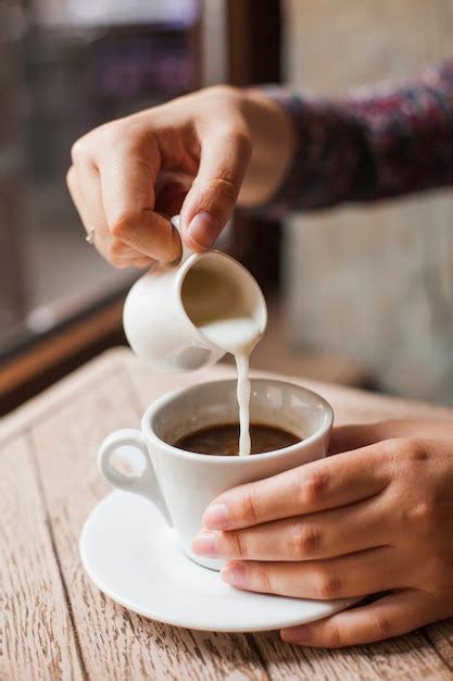 Close Up Of Female Hand Pouring Milk Into The Coffee Cup At Restaurant