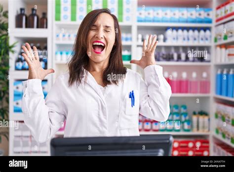 Middle Age Brunette Woman Working At Pharmacy Drugstore Celebrating Mad And Crazy For Success