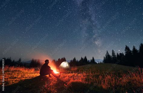 Plakat Silhouette Of Male Traveler Sitting Near Campfire Under Night