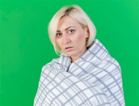 Confiant jeune femme malade blonde enveloppée de plaid regarde à l avant isolé sur mur vert