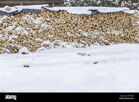 Firewood Stacked In Winter Wood Pile With Snow Stacked For Firewood