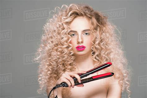 Beautiful Naked Girl With Long Curly Hair Holding Hair Straightener And Looking At Camera