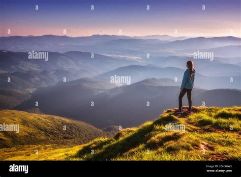 Girl On Mountain Peak With Green Grass Looking In Mountains Stock Photo