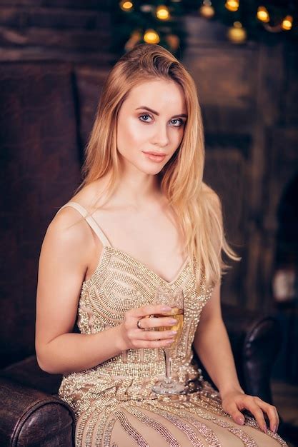 Belle femme blonde sexy porte une robe de soirée dorée garde à portée de main une coupe de