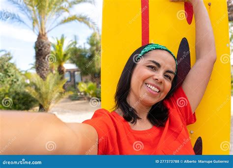 Smiling Latina Woman Taking A Selfie Next To A Surfboard On Her