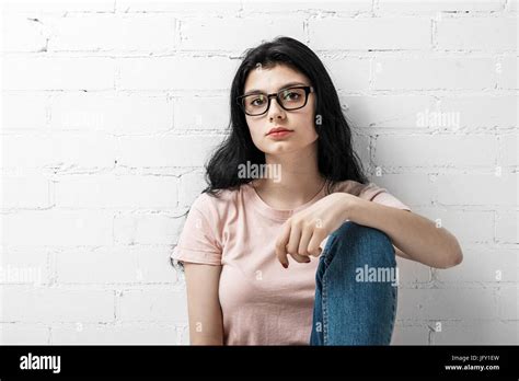Portrait Of Smart Beautiful Brunette Girl In Eyeglasses With Natural Make Up Sitting Near White