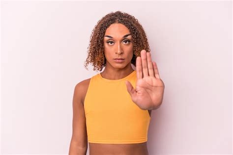 Jovem transexual latina isolada no fundo rosa em pé a mão estendida mostrando o sinal de