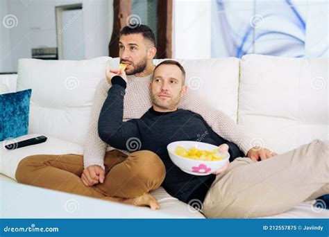 Pareja Gay Sentada En El Sof En Casa Viendo Algo En La Televisi N Y Comiendo Un Bocadillo