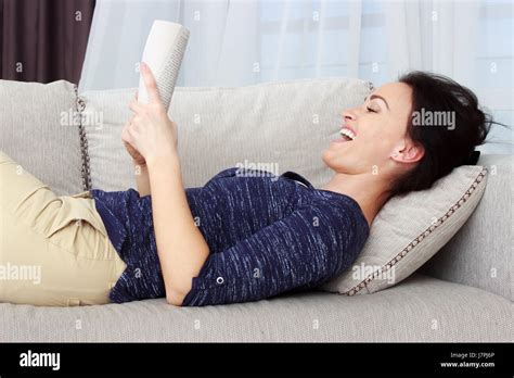 Smiling Beautiful Brunette Relaxing On The Couch And Reading A Book In The Living Room Stock