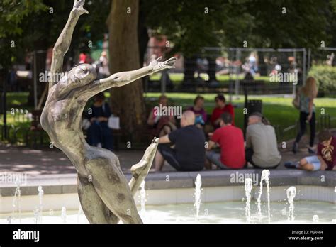 People Relaxing In The Shadow Behind Statue Of A Nude Woman Dancing Elegantly In A Fountain In