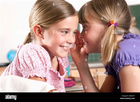 two young girls whispering to each other in classroom Stock Photo - Alamy