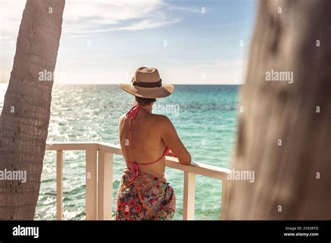 Back View Of Unrecognizable Woman In A Straw Hat And Red Bikini Top Admiring The Caribbean Sea