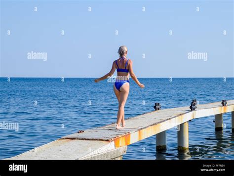 Ein schönes Mädchen in einem blauen Bikini geht den Pier zum Meer Marine Betonpfeiler Ins