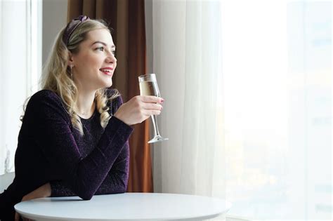 Une Belle Fille Blonde En Robe Tient Un Verre De Champagne Dans Ses Mains Sourit Et Regarde Par