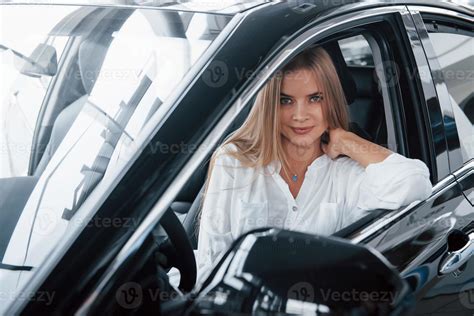 en chemise blanche belle fille blonde assise dans la nouvelle voiture avec un intérieur noir