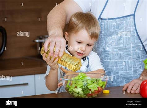 The Blonde Haired Son And Father Prepare A Salad Of Colorful Fresh Vegetables Together In The