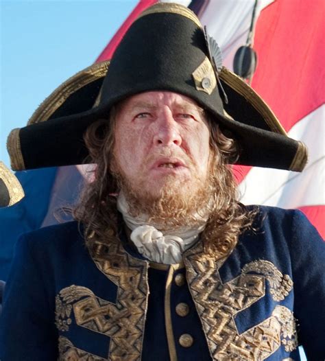 a man with long hair wearing a black hat and blue coat standing in ...