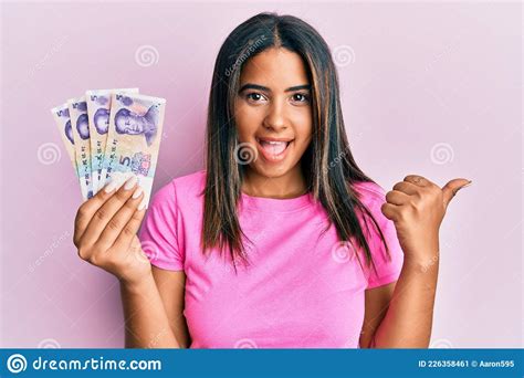 Jovem Latina Segurando Notas Yuans Chinesas Apontando O Polegar Para O Lado Sorrindo Feliz A