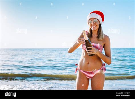 Belle femme blonde en bikini rouge et chapeau de père Noël avec champagne debout sur une plage