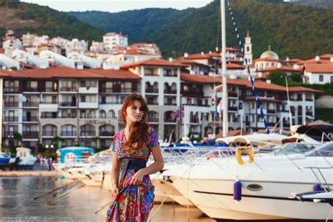 Attractive Brunette In Long Colorful Dress Standing Alone On The Beach Against The Backdrop Of