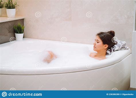 Young Woman Lies In White Bath Of Foam With Her Eyes Closed Spa