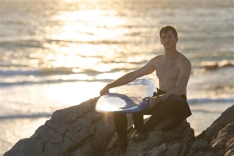 Premium Photo Fit Man With Naked Torso Sitting On The Rock At The Seashore Holding A Surfboard