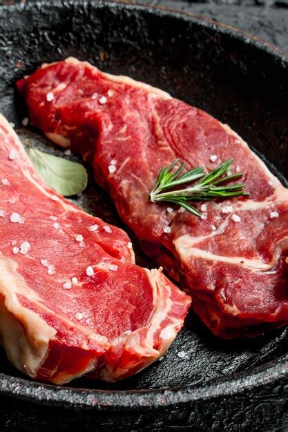 Premium Photo Raw Beef Steaks In An Old Pan With Rosemary Sprig